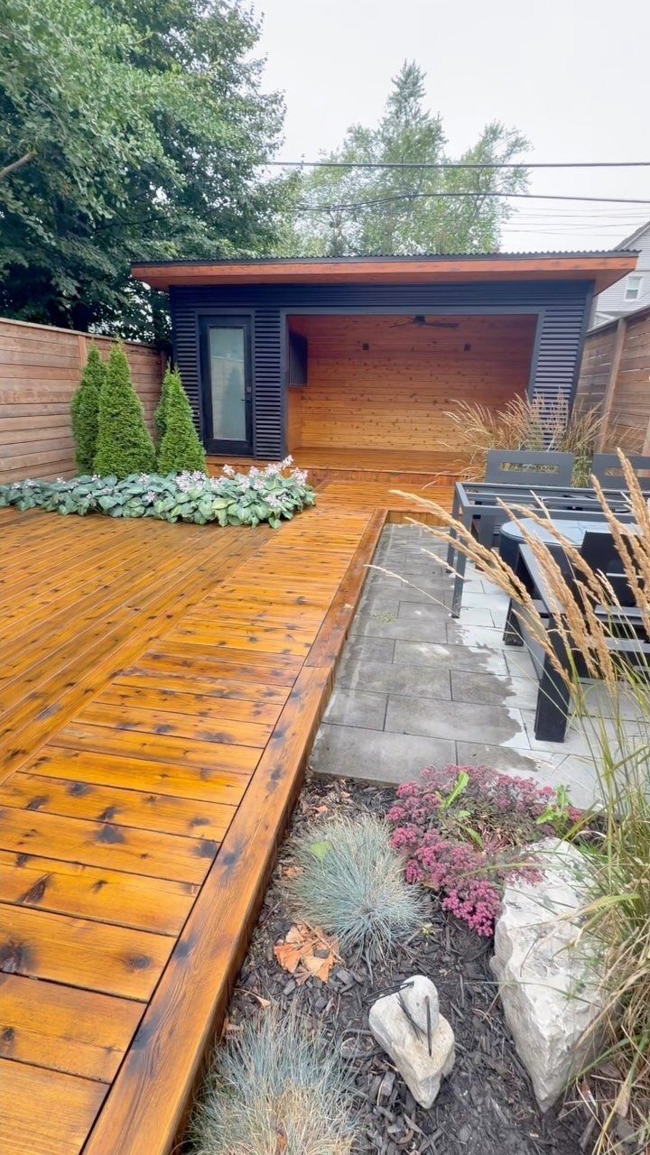 Decks de Madeira: 7 Ideas for Outdoor Living Spaces 2 Polished honey-colored wooden deck planks extending towards a dark wooden garden structure and stone patio.
