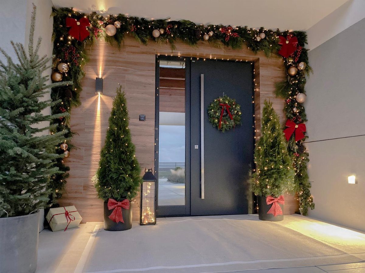 Decorating for Christmas: 12 Ideas That Work in Real Rooms 11 A decorated entryway with a wreath on the door and a garland framing the wooden wall.