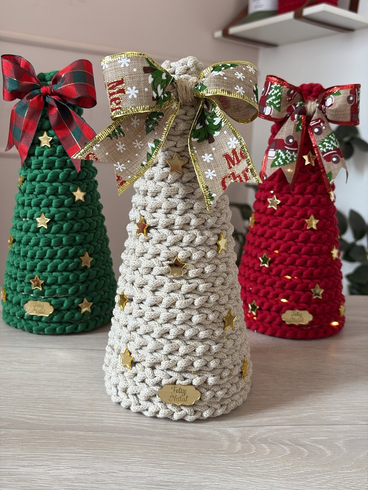 Three braided yarn Christmas trees in green, cream, and red decorated with gold stars and bows.