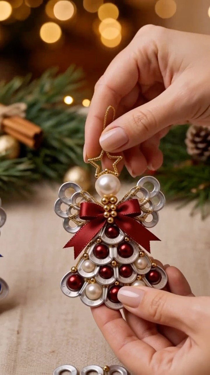 Hands holding a handmade angel ornament crafted from soda can tabs, pearls, and a red bow.