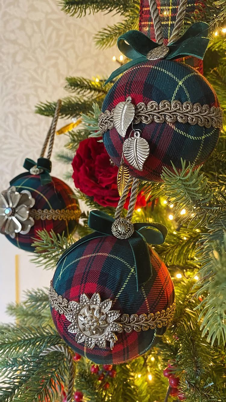 Plaid fabric Christmas ornaments with silver metallic decorations hanging on a lit evergreen tree.