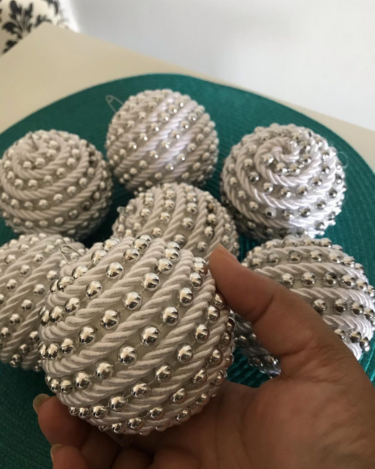 White spherical ornaments decorated with silver beads and rope patterns held in a person's hand.