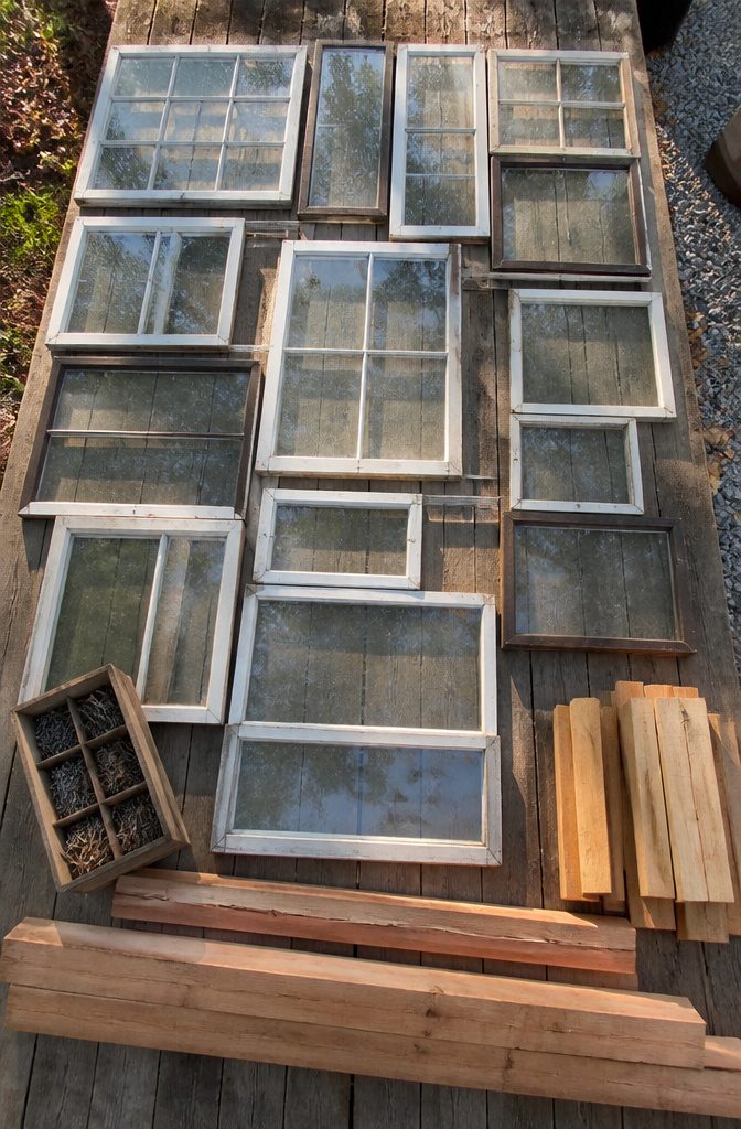 A collection of old windows stacked for a DIY greenhouse.