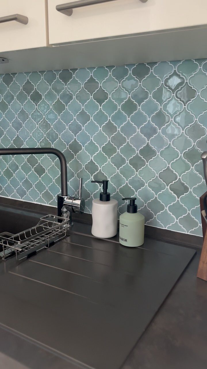 Teal arabesque patterned backsplash tiles above a dark grey kitchen countertop with a black faucet.