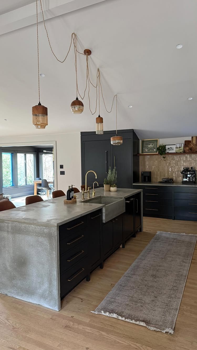 Grey concrete countertops on a large kitchen island with dark cabinets and light wood floors.