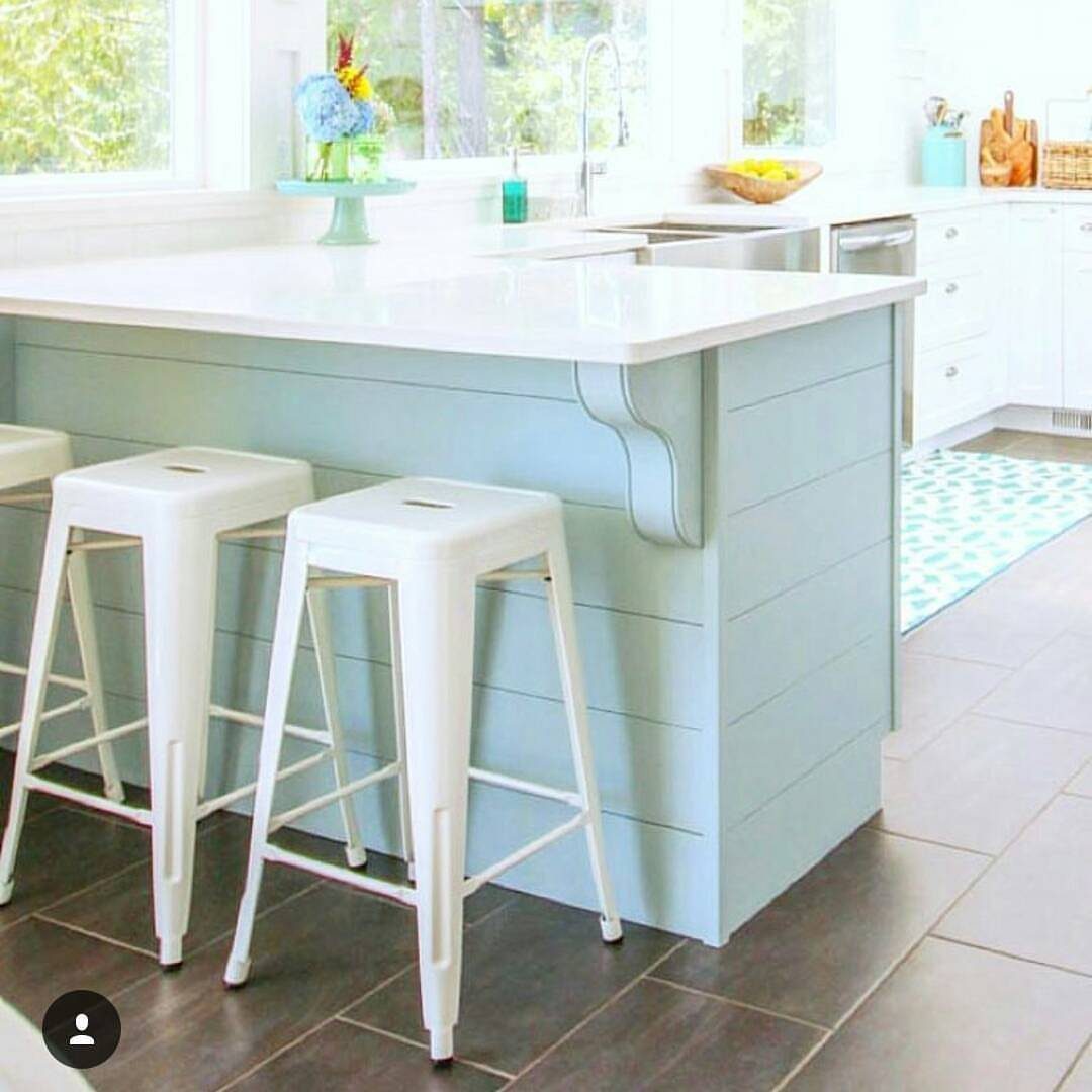 Light blue kitchen peninsula with horizontal planking and white bar stools in a bright kitchen.