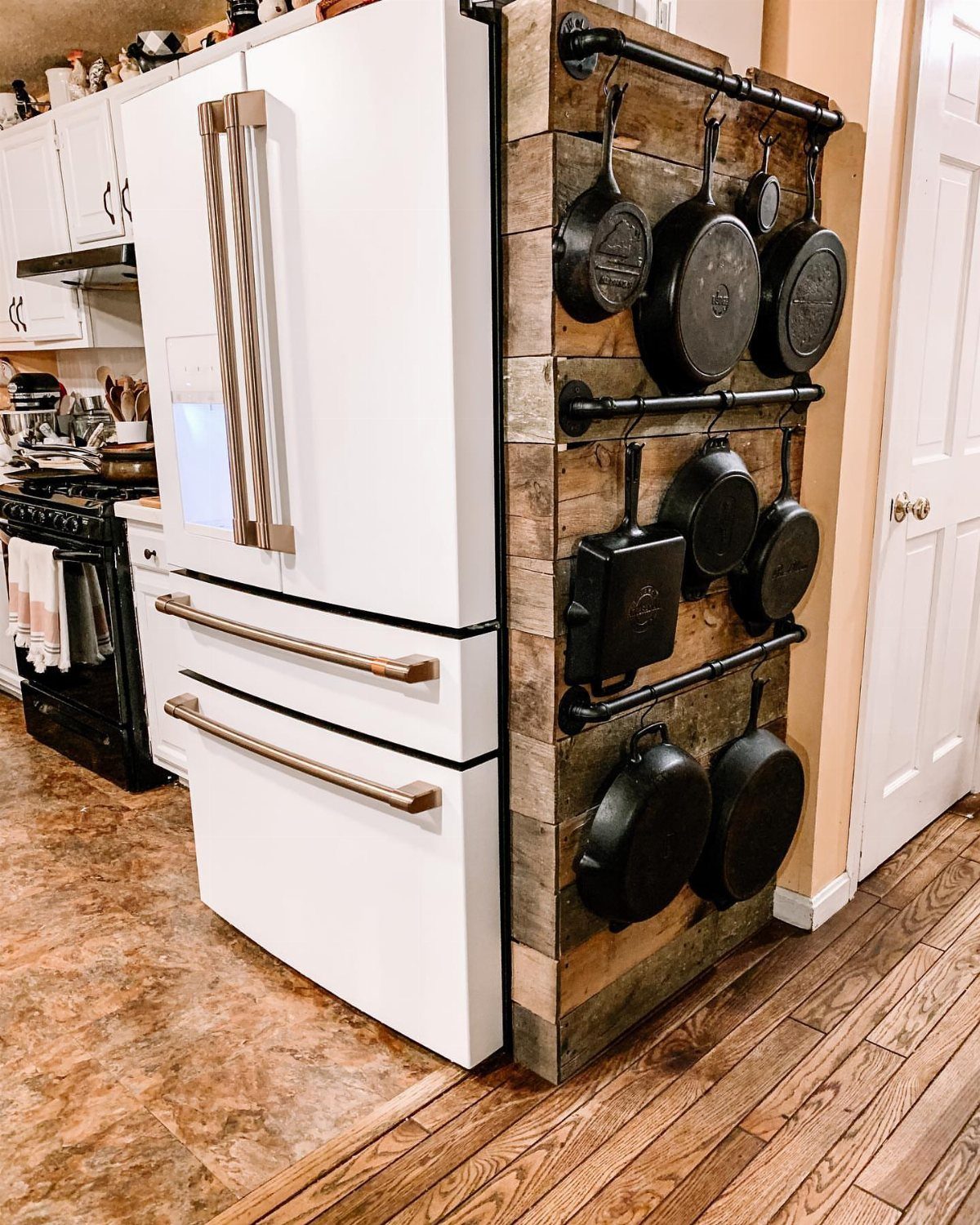 Cast iron pans hanging from black metal rails on a rustic wooden kitchen wall panel.
