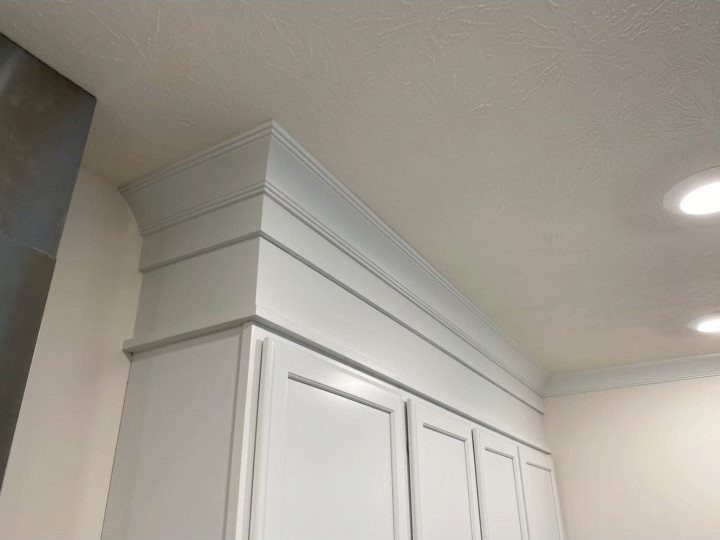 White kitchen cabinets with decorative crown molding installed against a white ceiling.