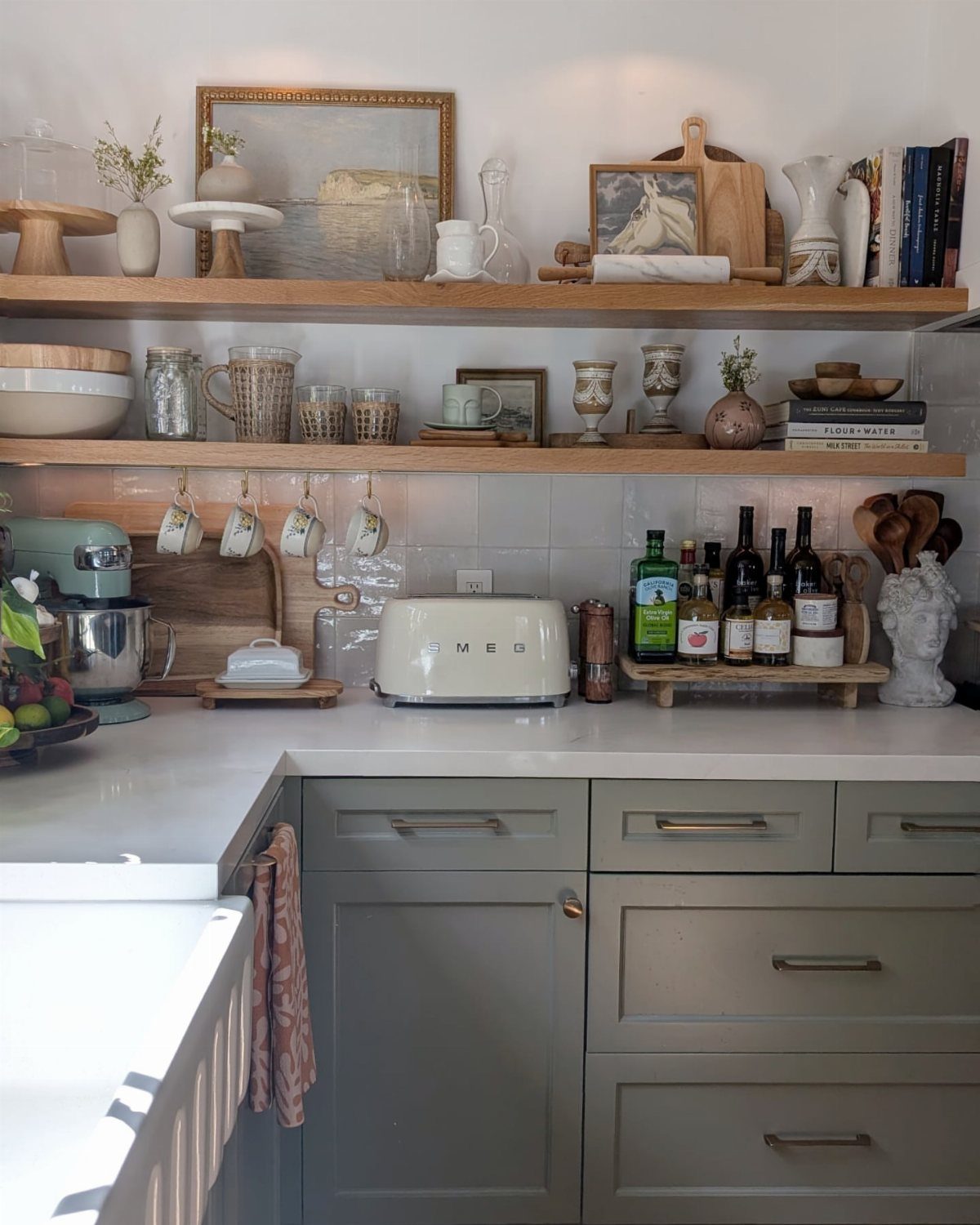 Wooden floating shelves holding various kitchenware, glassware, and decorative items against a white tiled wall.