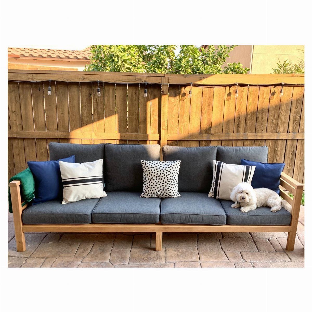 DIY Patio Couch: 8 Projects to Build for Any Budget 5 A wooden outdoor sofa with grey cushions and colorful pillows on a stone patio.