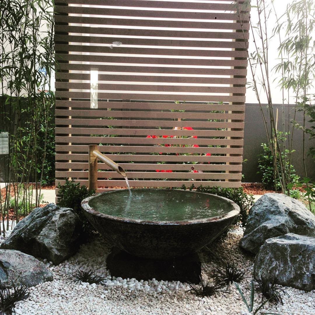 Easy Garden DIY: 18 Projects for a Yard That Feels Finished 11 Bamboo spout pouring water into a large stone basin surrounded by rocks and white pebbles.