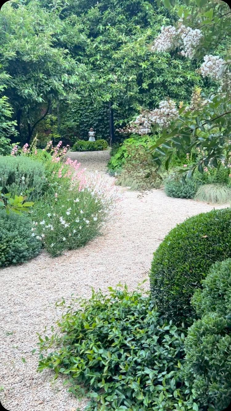 Easy Garden DIY: 18 Projects for a Yard That Feels Finished 7 A winding gravel path curves through a lush garden filled with green shrubs and white flowers.
