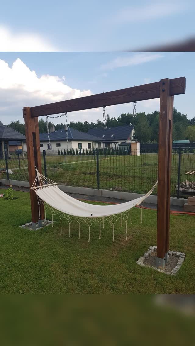 Easy Garden DIY: 18 Projects for a Yard That Feels Finished 8 A white fabric hammock suspended between two large dark wooden posts on a green lawn.