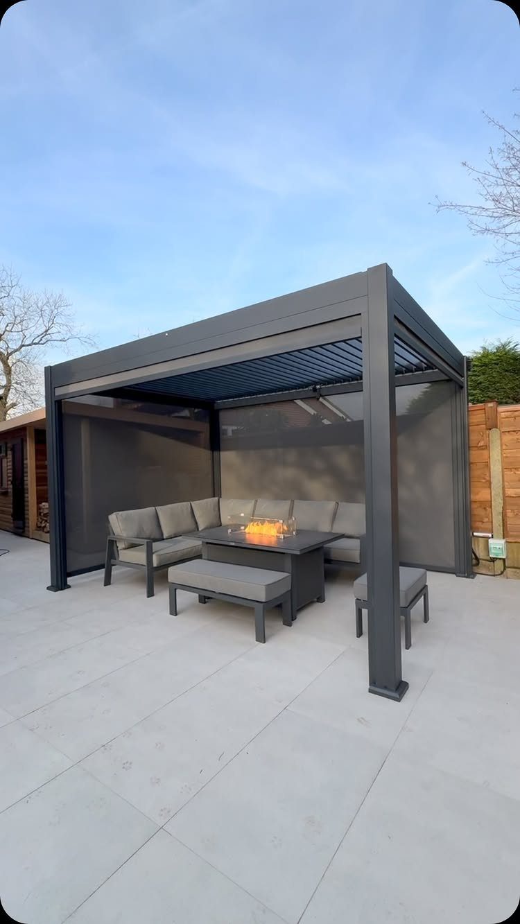 Easy Garden DIY: 18 Projects for a Yard That Feels Finished 12 Dark grey metal square pergola enclosing a modern outdoor lounge set with a fire pit table.
