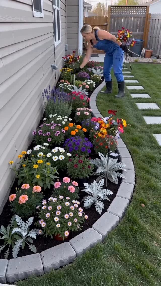 A woman gardening in a colorful flower bed lined with grey stone edging blocks.