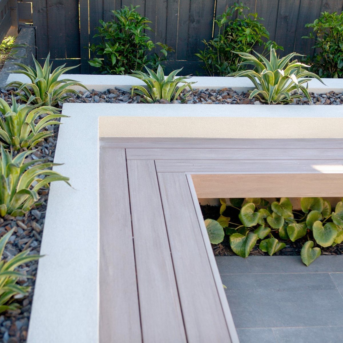10 Front Yard Decks Ground Level That Welcome Guests First 1 Built-in wooden bench seating integrated into a modern concrete garden structure with green plants.