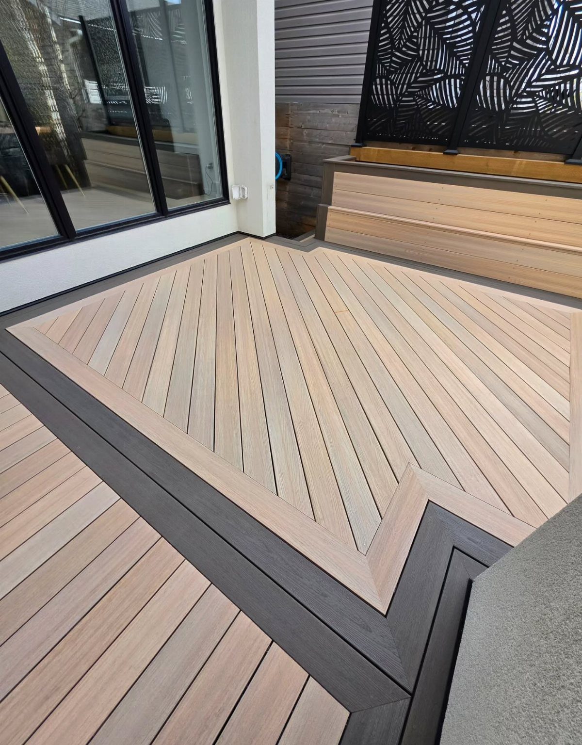10 Front Yard Decks Ground Level That Welcome Guests First 8 Light tan wooden deck with chevron pattern and dark grey borders next to a building.