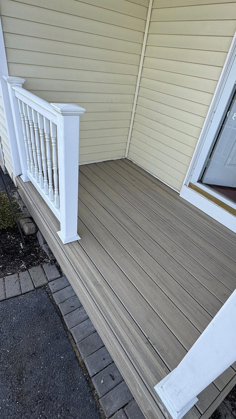 10 Front Yard Decks Ground Level That Welcome Guests First 6 A light brown composite deck with white railings next to a beige house and brick path.
