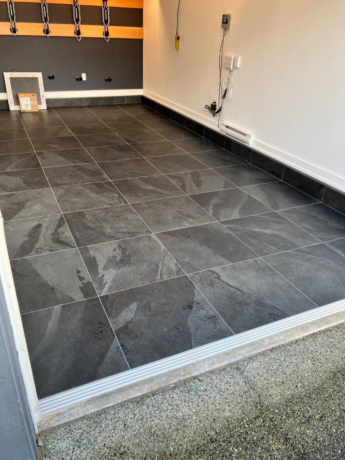Dark grey porcelain tiles with a stone texture covering a clean garage floor.