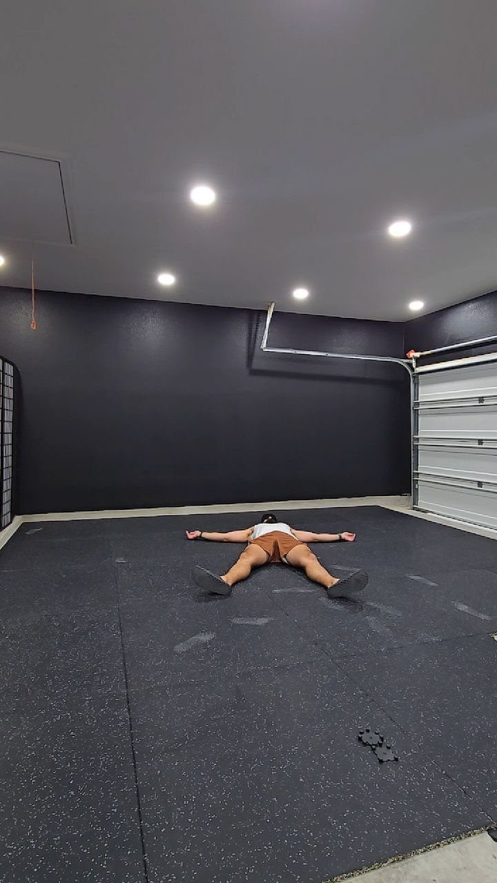 A person lying on dark speckled rubber flooring tiles in a modern garage.
