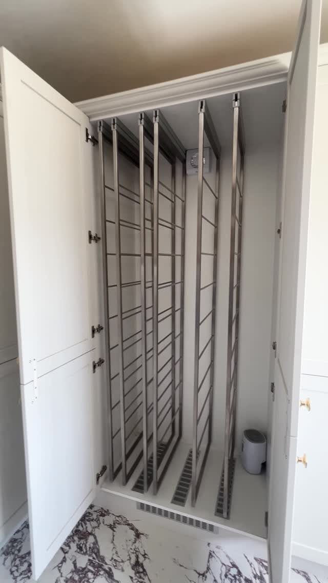Vertical metal drying racks installed inside a white built-in closet with marble flooring.
