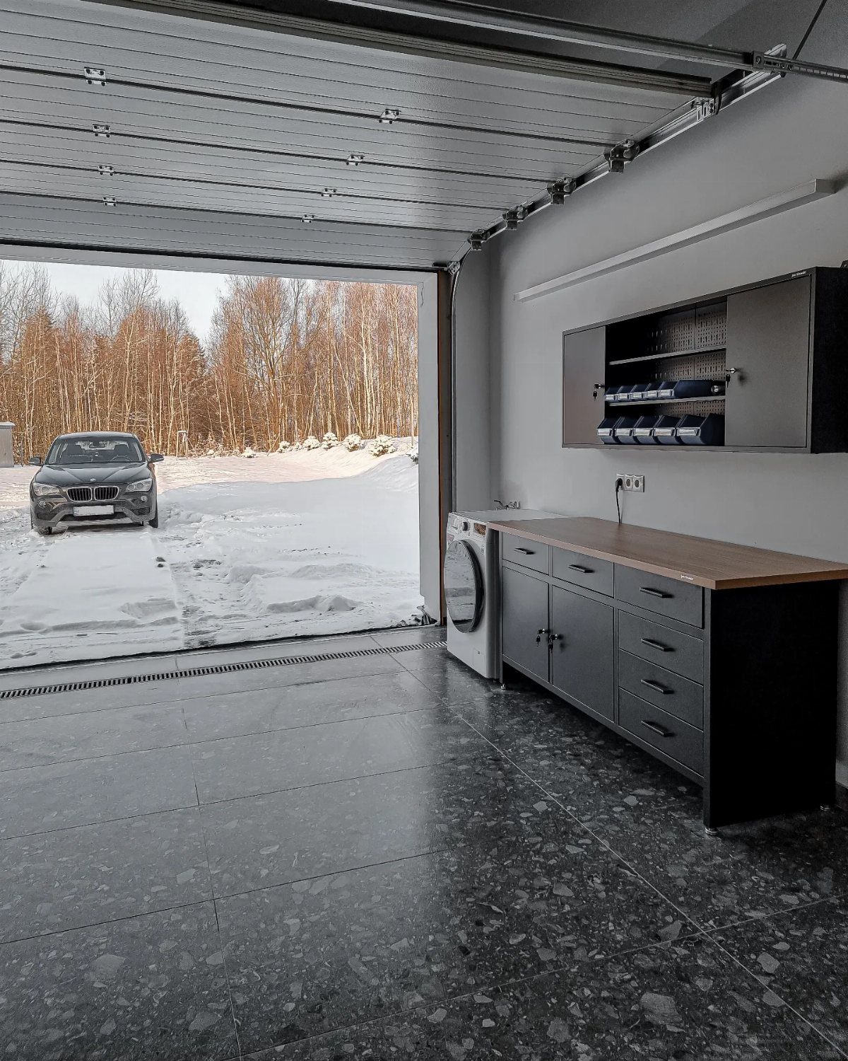 Grey cabinets with a wooden countertop and a washing machine in a modern garage space.