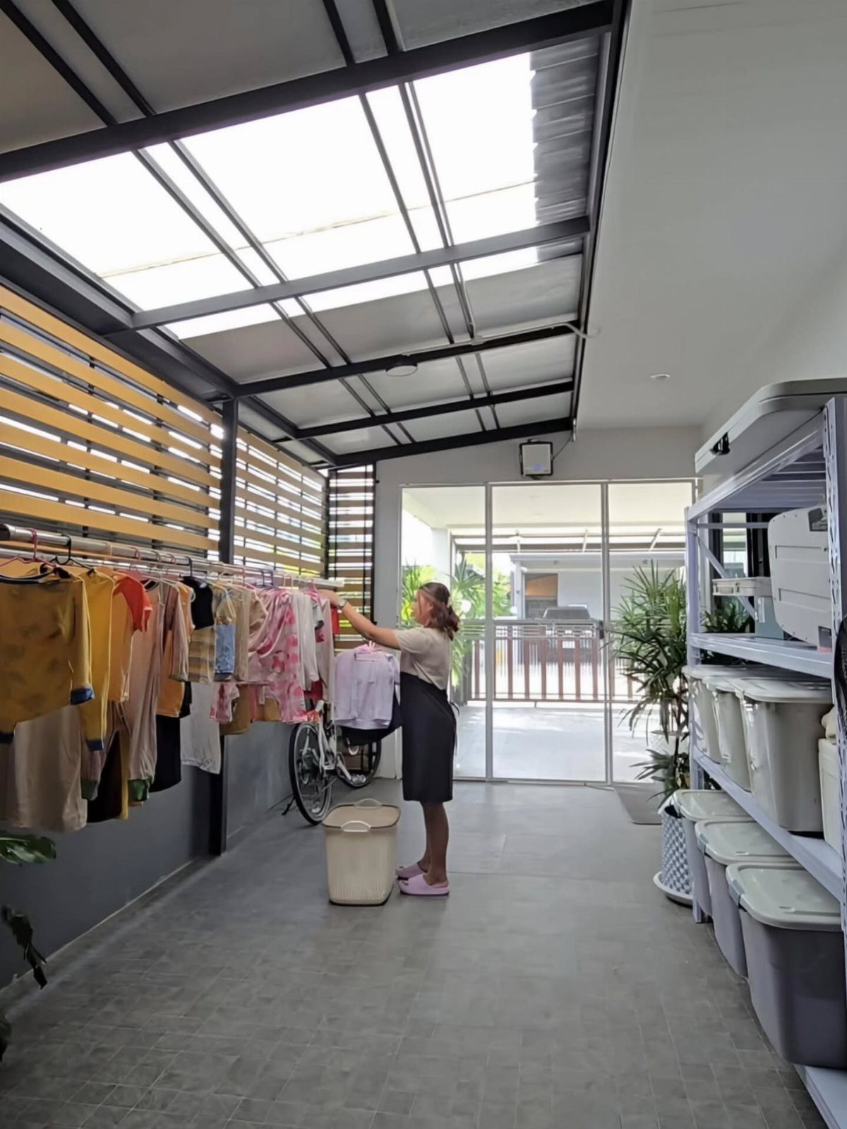 Woman hanging clothes on a rack under a large translucent skylight in a bright utility room.