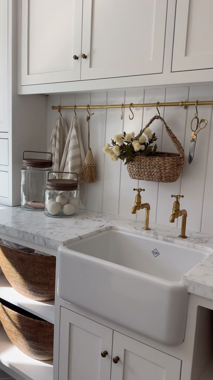 White farmhouse sink with marble countertop and gold faucets against white beadboard walls.