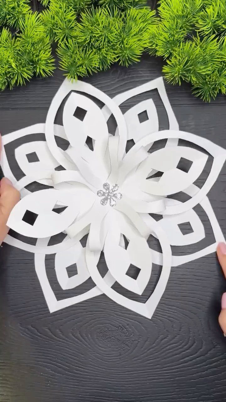 White paper snowflake ornament with intricate cutouts and a central gem on dark wood.