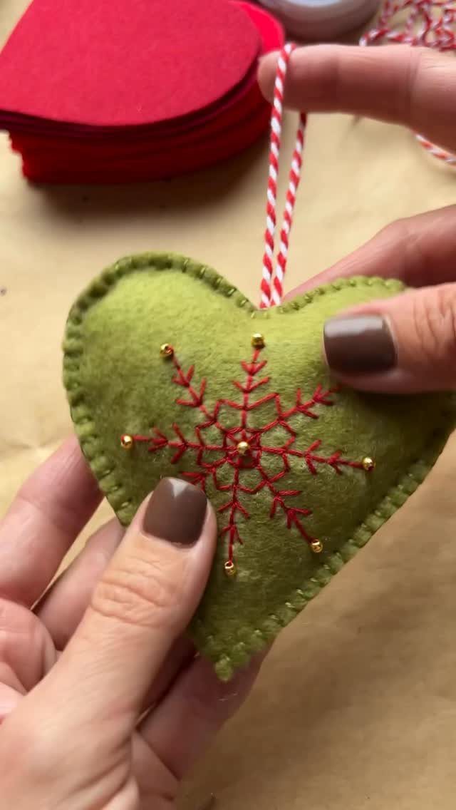 Hands holding a green felt heart ornament with a red embroidered snowflake design.