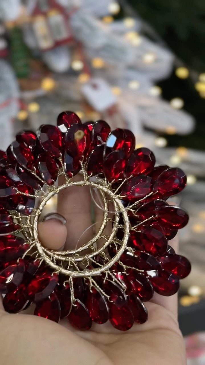 A hand holding a circular ornament made of faceted red jewel beads and gold wire.