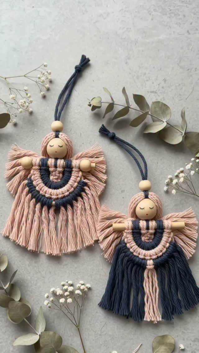 Two macrame angel ornaments with wooden beads and pink and navy fringe on a grey background.