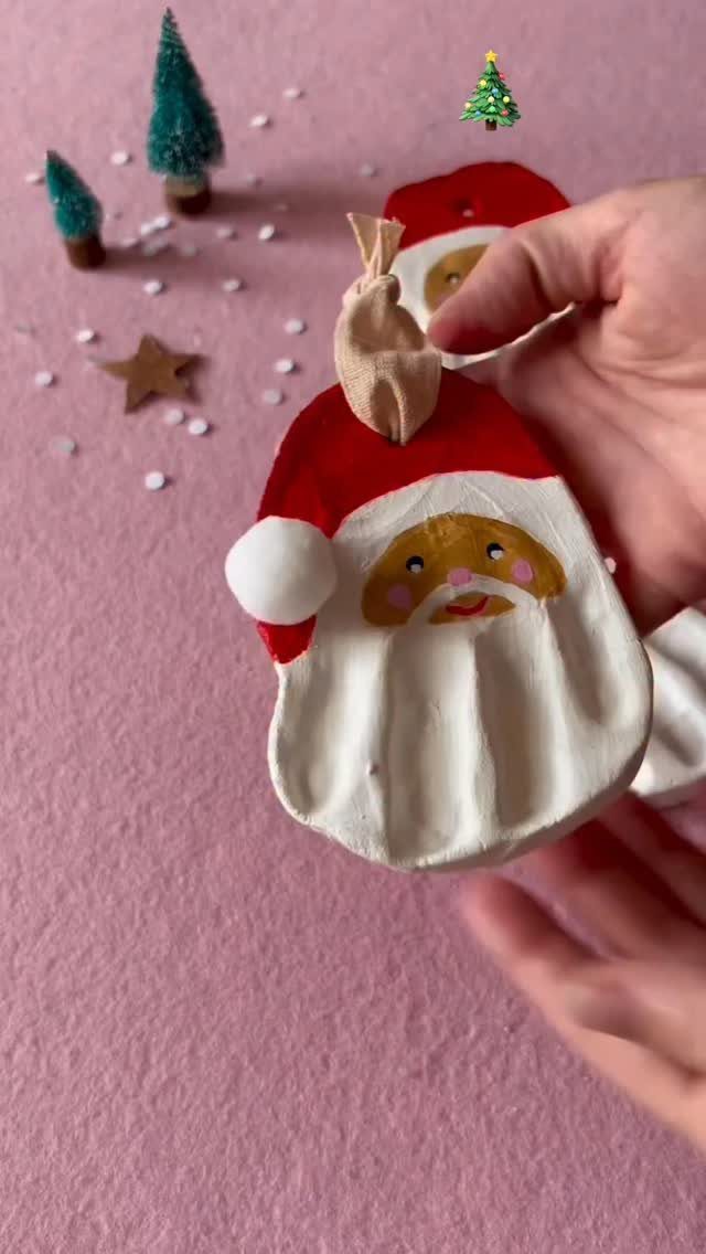 A hand holding a white salt dough Santa Claus ornament against a pink background.