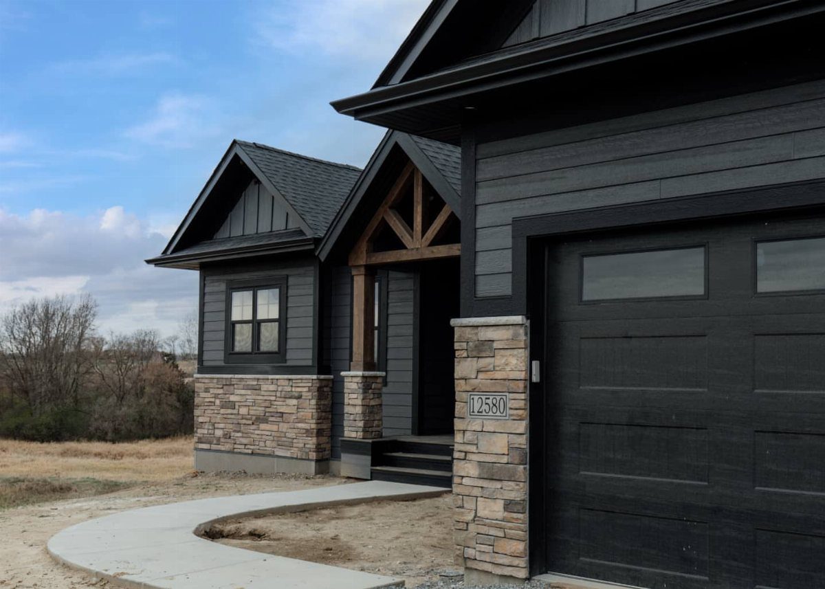 Modern house with black siding, stone accents, and a black garage door under a blue sky.