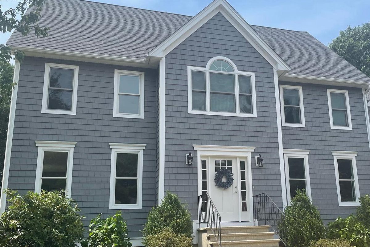 Charcoal gray shingle siding on a two-story house with white window trim and a white door.