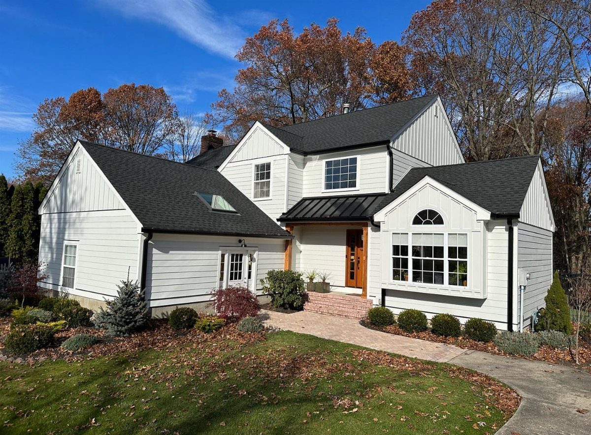 A white house with black trim and roofing, featuring horizontal and vertical siding under a blue sky.