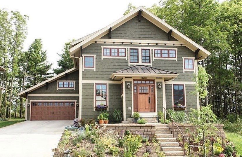 A two-story house featuring dark sage green siding with cream trim and wooden doors.