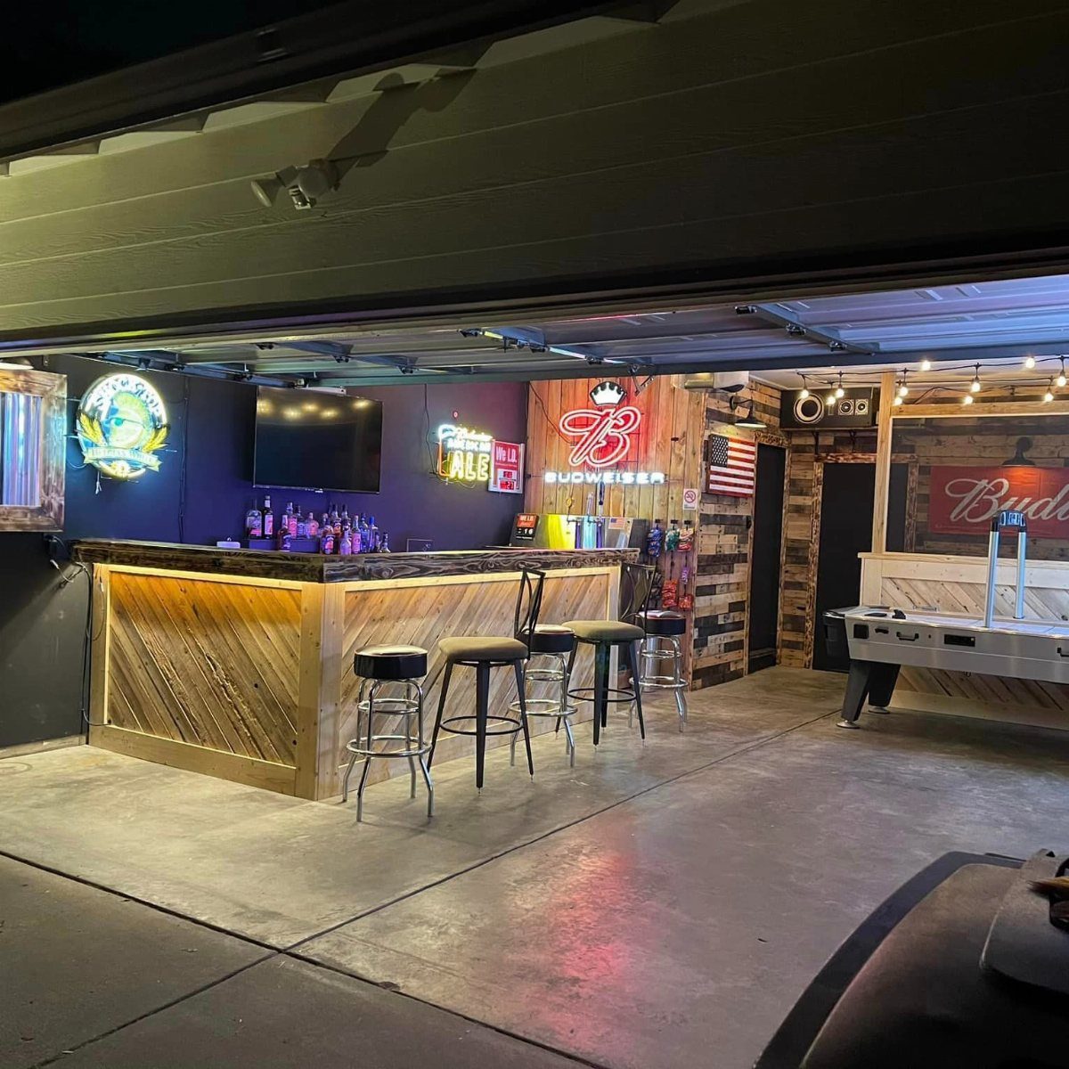 9 Multi Use Garage Ideas for Living, Work, and Play 5 A wooden bar counter with stools and neon signs inside a converted garage space.