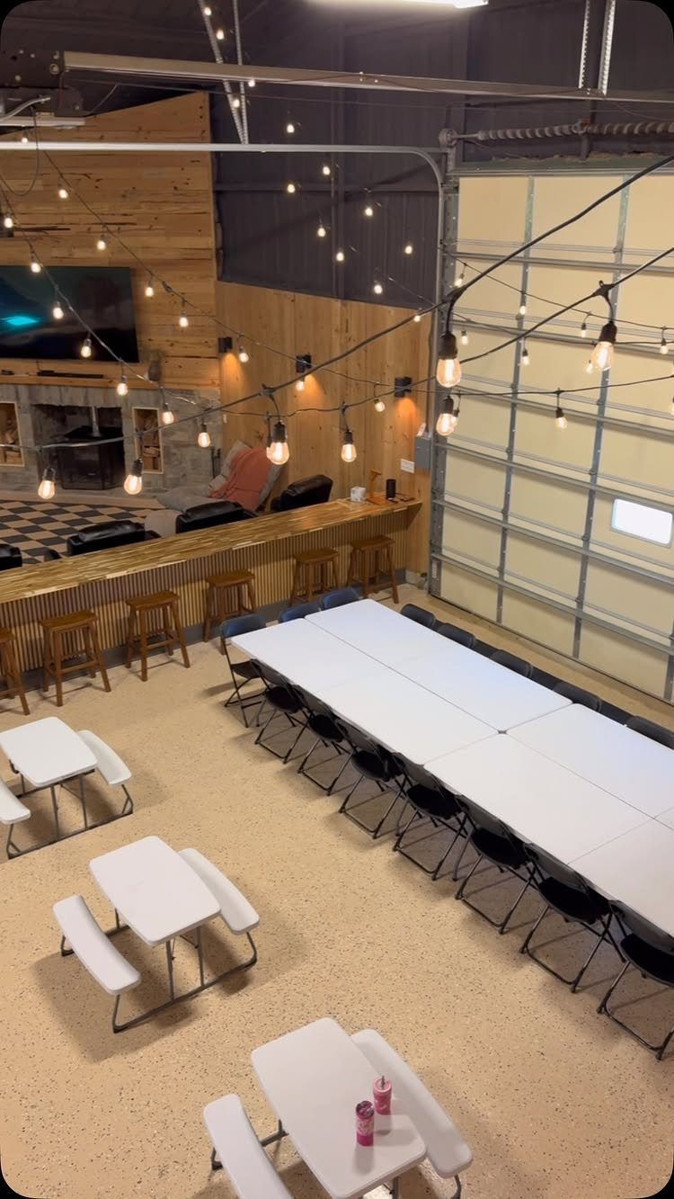 9 Multi Use Garage Ideas for Living, Work, and Play 9 A large converted garage space with a long white table, wooden bar, and string lights.