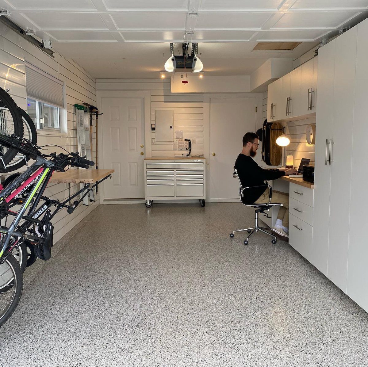 9 Multi Use Garage Ideas for Living, Work, and Play 2 A man working on a laptop at a built-in white desk inside a clean, organized garage.
