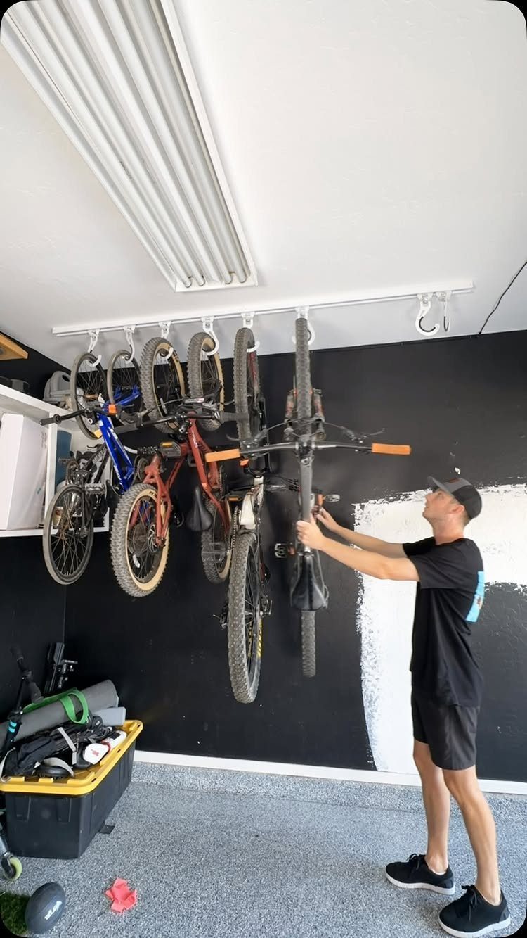 9 Multi Use Garage Ideas for Living, Work, and Play 7 A man hanging a bicycle onto a white ceiling-mounted storage rack in a garage.