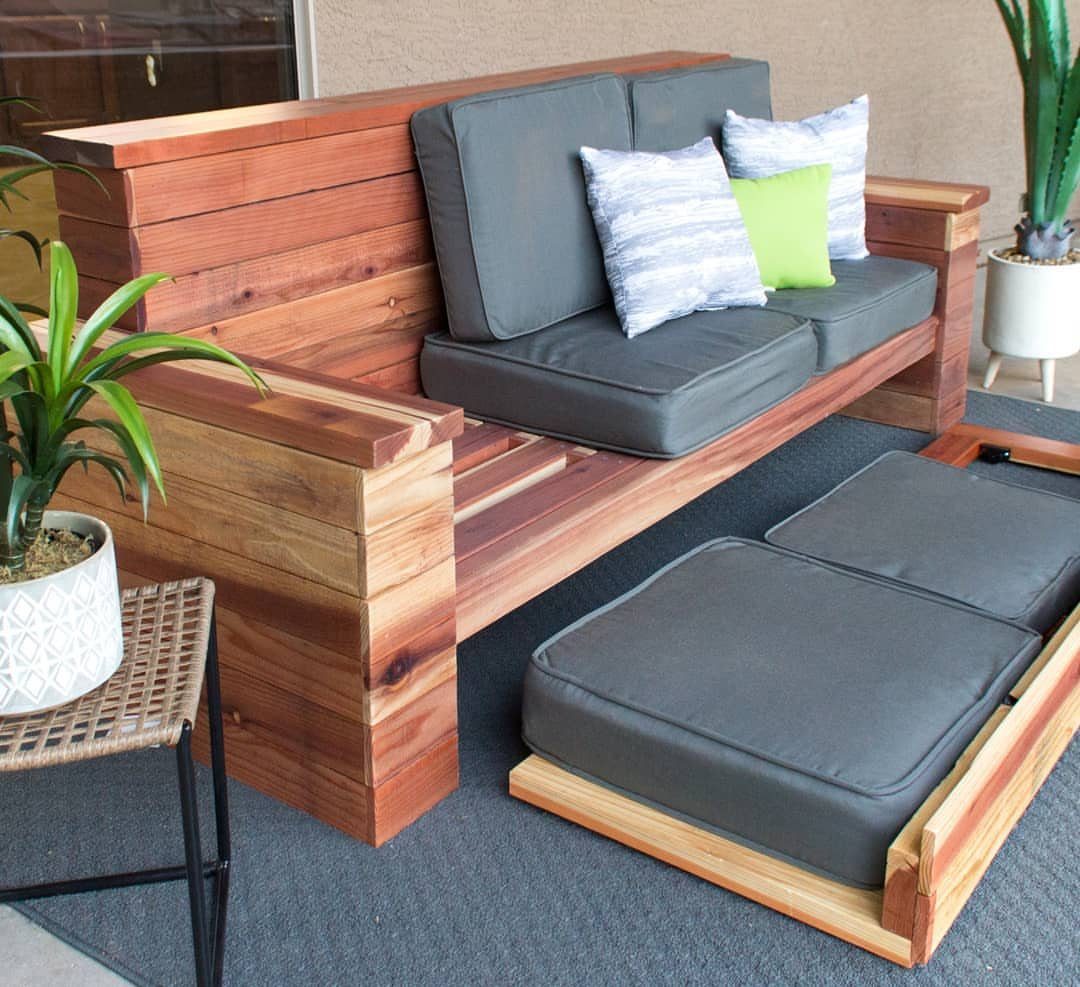 A handmade wooden outdoor sofa with grey cushions and colorful pillows on a patio.