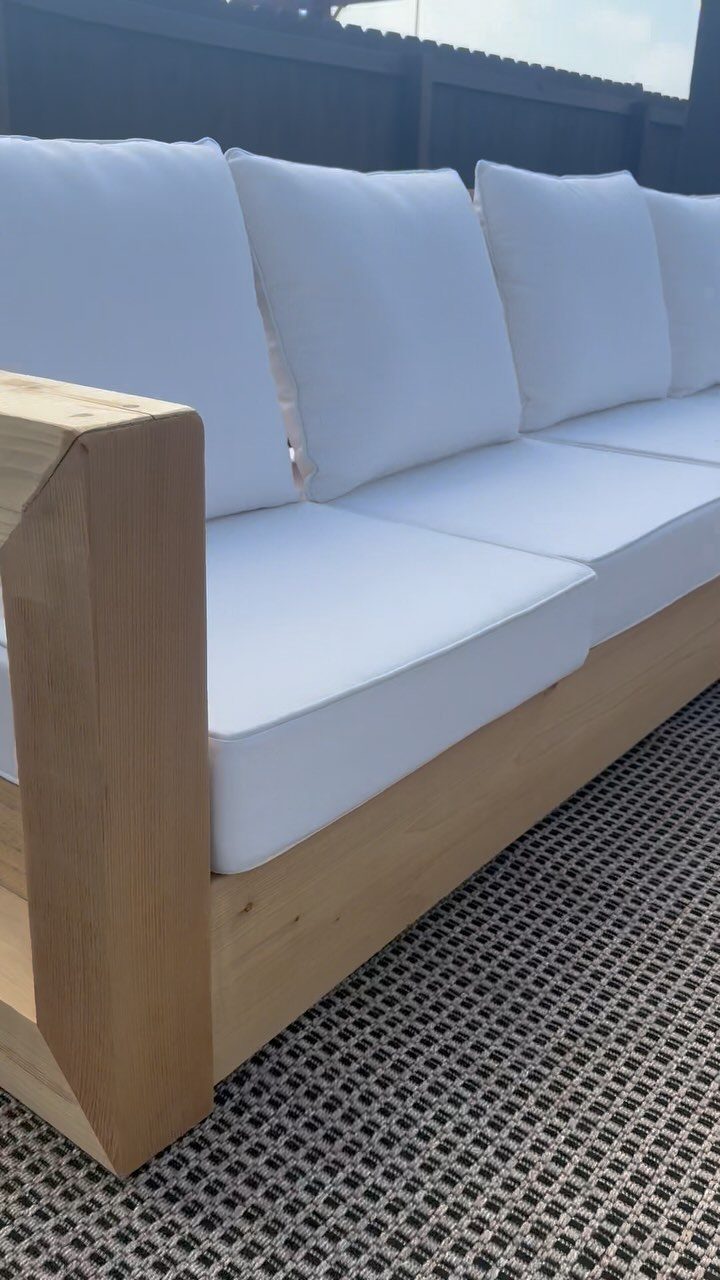 A light wood outdoor sofa with large white cushions sitting on a patterned rug.