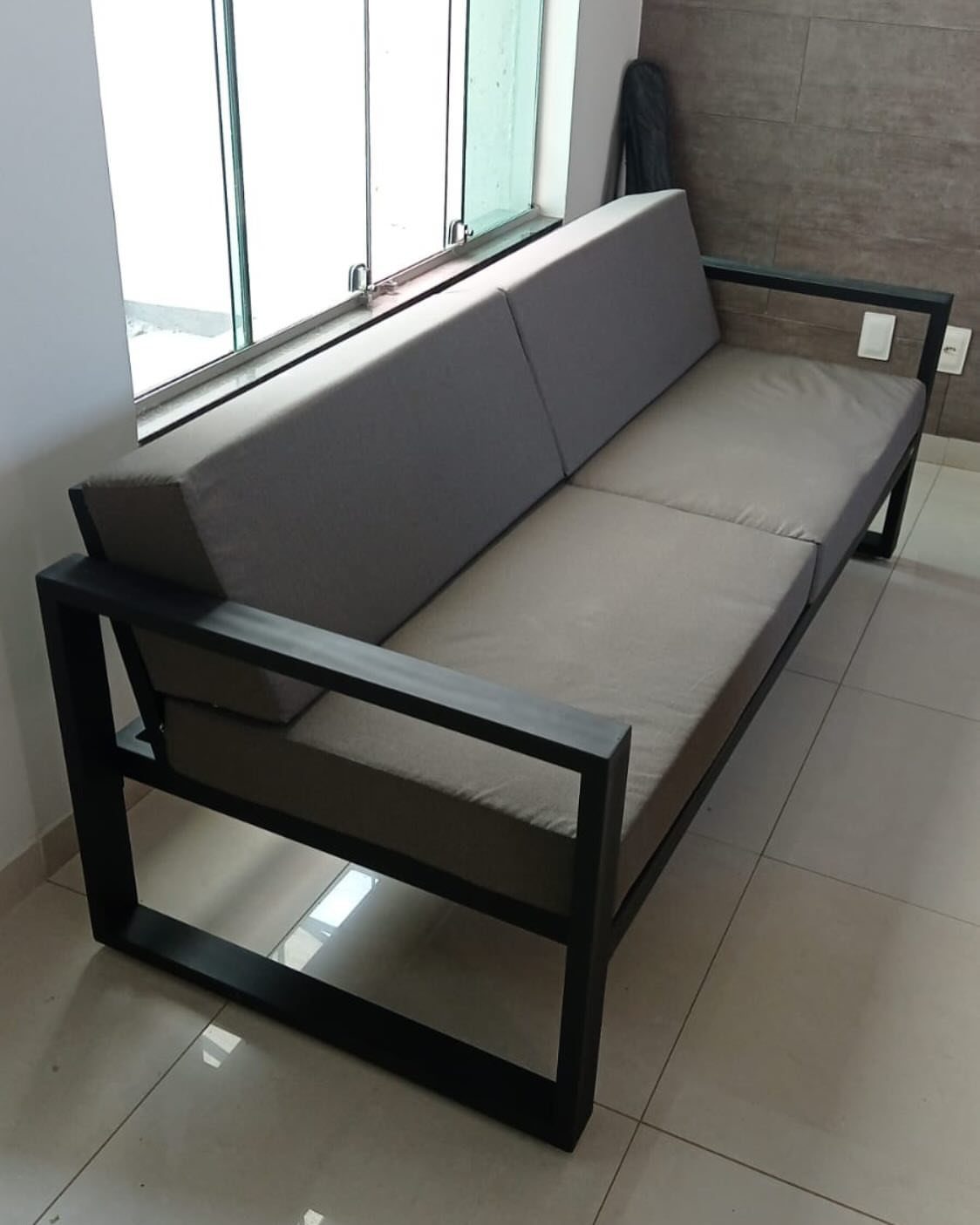 A modern black metal frame sofa with grey cushions sitting next to a large window.