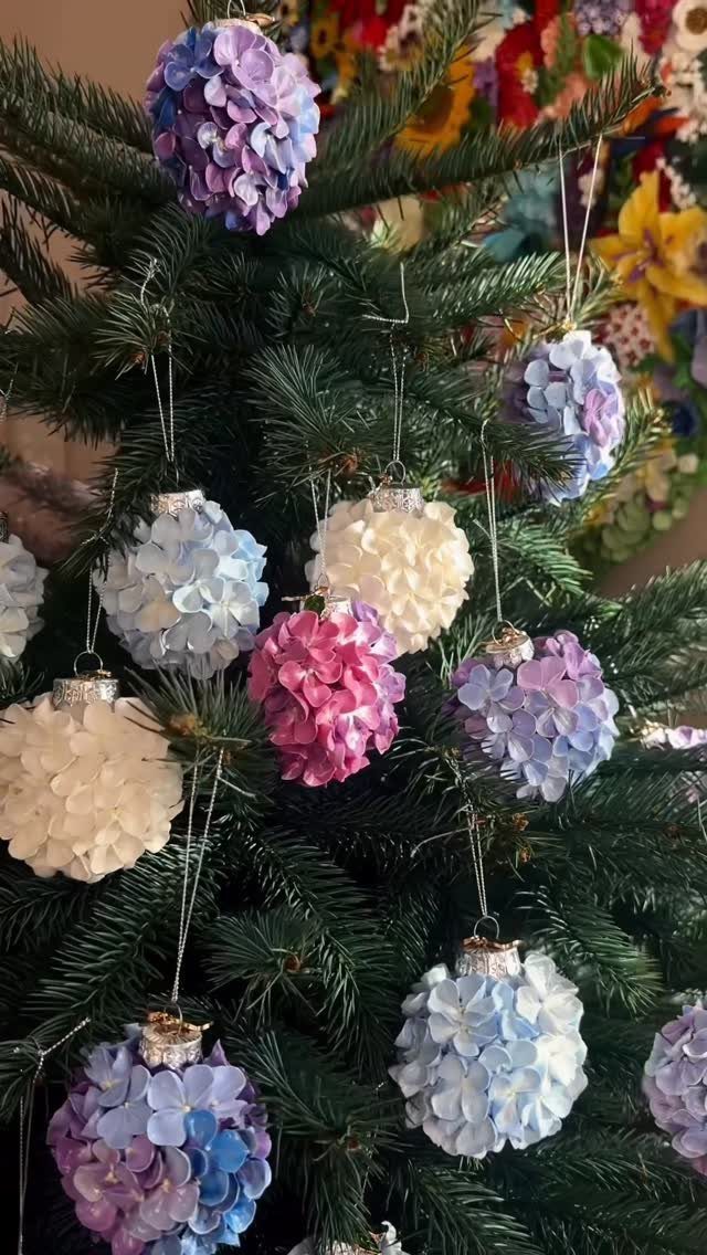 Floral petal ornaments in shades of purple, pink, and white hanging on a green Christmas tree.