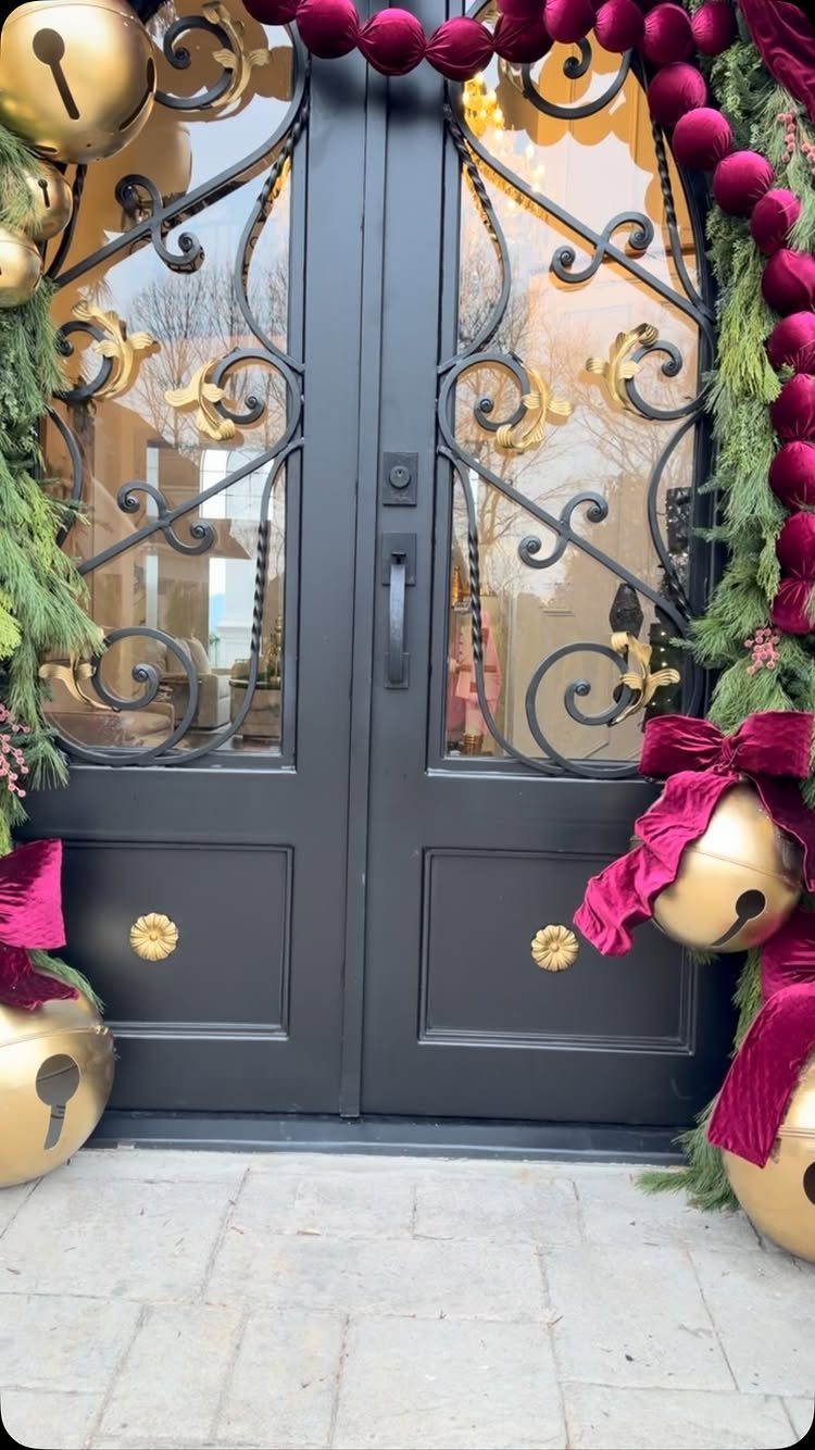 Dark grey double doors decorated with green pine garlands, gold bells, and purple velvet ornaments.